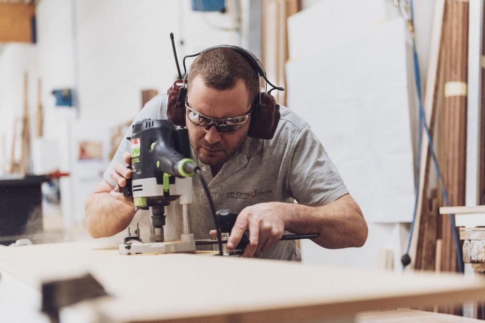 Ateliermedewerker De Laere Decor is hout aan het bewerken en draagt een veiligheidsbril